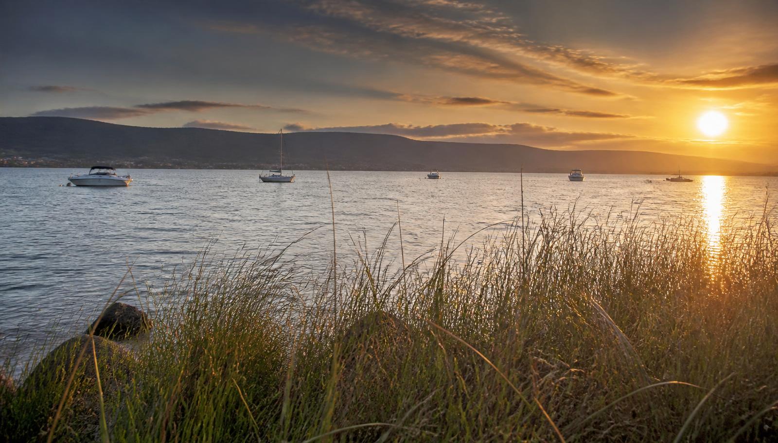 Licensed plumber and electrician servicing Dombarton — sunset over Lake Illawarra with moored boats and the escarpment beyond Dapto, Wollongong NSW.